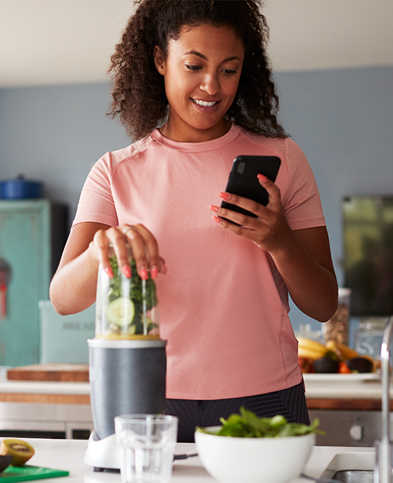 Woman making a smoothie and referencing her phone for the toolkit.